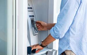 hands and torso of person putting their debit card into an ATM