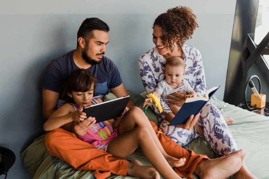 Família com duas crianças pequenas usando o laptop na cama
