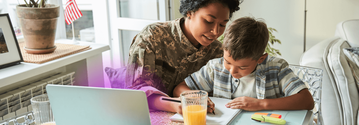 Madre e hijo sentados a una mesa dibujando en un papel con un ordenador portátil abierto delante de ellos. La madre lleva uniforme militar.
